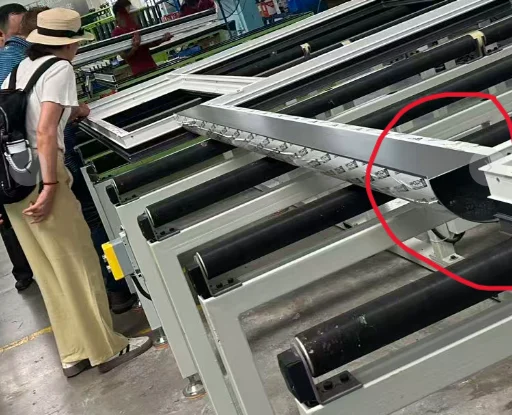 An assembled aluminium frame corner resting on a roller table on a factory floor, with a red circle drawn around the joint