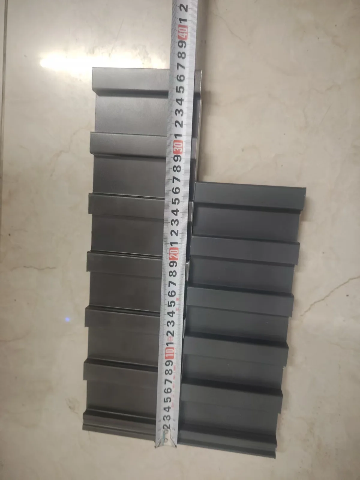 Two stacks of grey metal roof panel samples standing upright beside a vertical tape measure